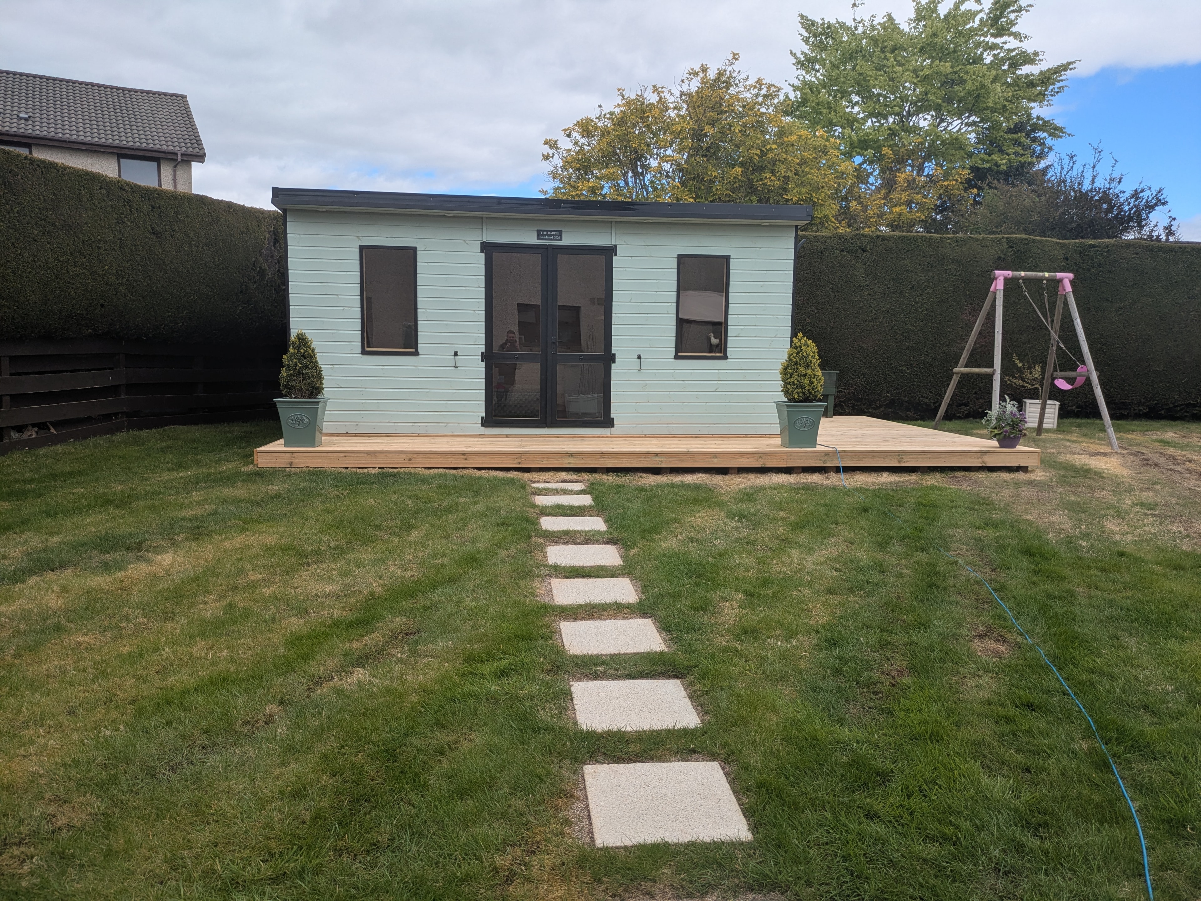 Light blue clad garden room with decking and stepping stone path