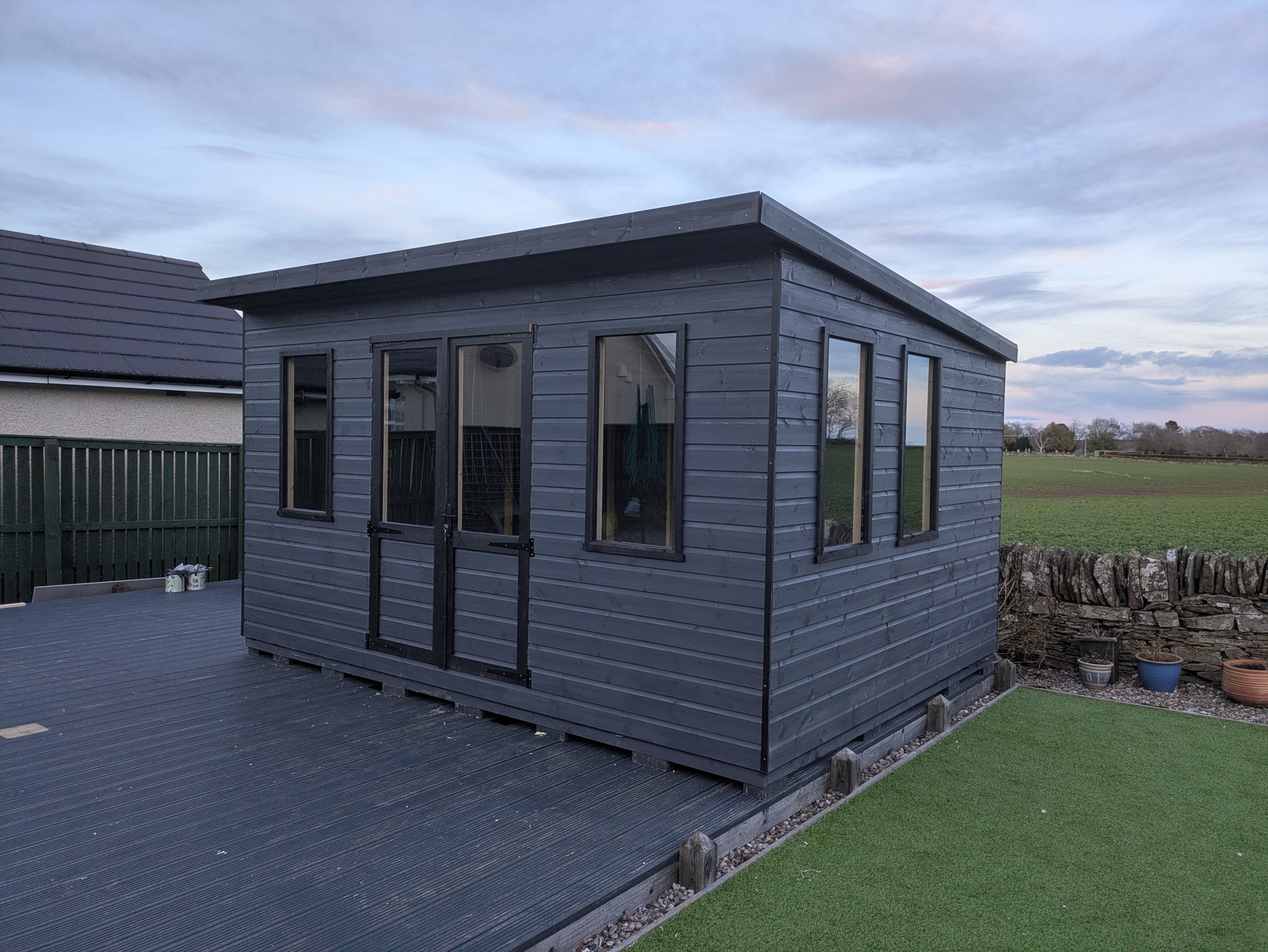Dark grey clad garden room with large windows and decking at dusk